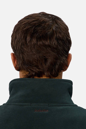 A person with short brown hair is shown from behind, wearing a dark green Industrie The New Luton Track Top with "Industrie" embroidered on the collar.