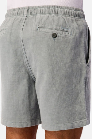Close-up of the back and side of a person wearing Industrie The New Mallorca Short in light grey textured cotton, featuring an elastic waistband, two back pockets—one with a button—and side pockets. These lightweight, breathable men’s shorts are crafted for both comfort and style.