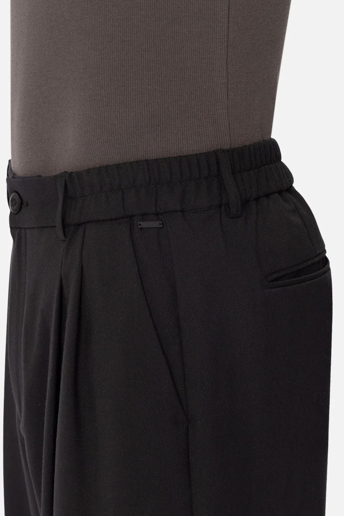 Side view of a person wearing Industrie The New Milano Pant in black, featuring an elastic waistband and side pockets. The focus is on the waist and upper hip, showcasing the comfortable fit with a dark top tucked in.
