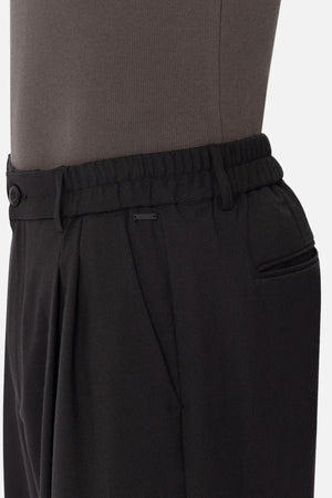 Side view of a person wearing Industrie The New Milano Pant in black, featuring an elastic waistband and side pockets. The focus is on the waist and upper hip, showcasing the comfortable fit with a dark top tucked in.