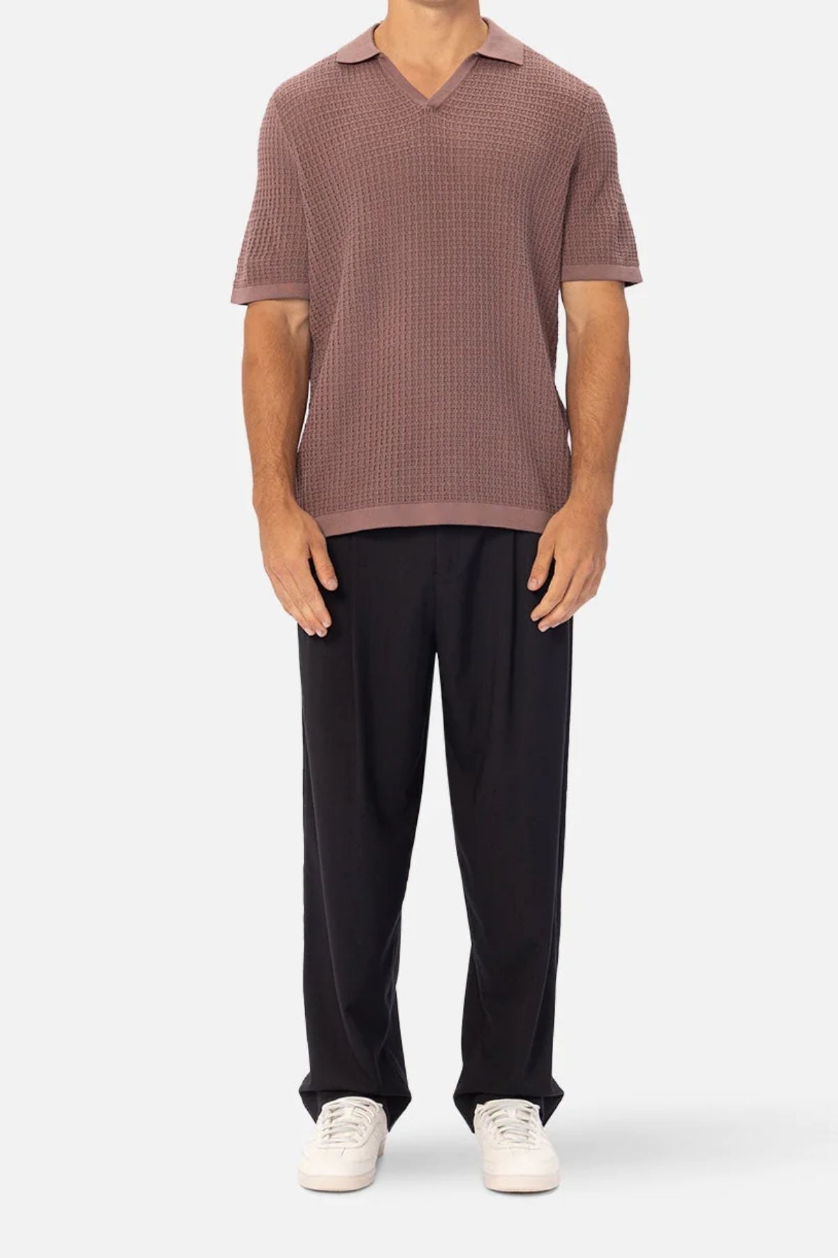 A man, head not visible, stands facing forward in a textured mauve collared short-sleeve sweater, Industrie The New Milano Pant black trousers for comfort, and white sneakers against a plain light background.