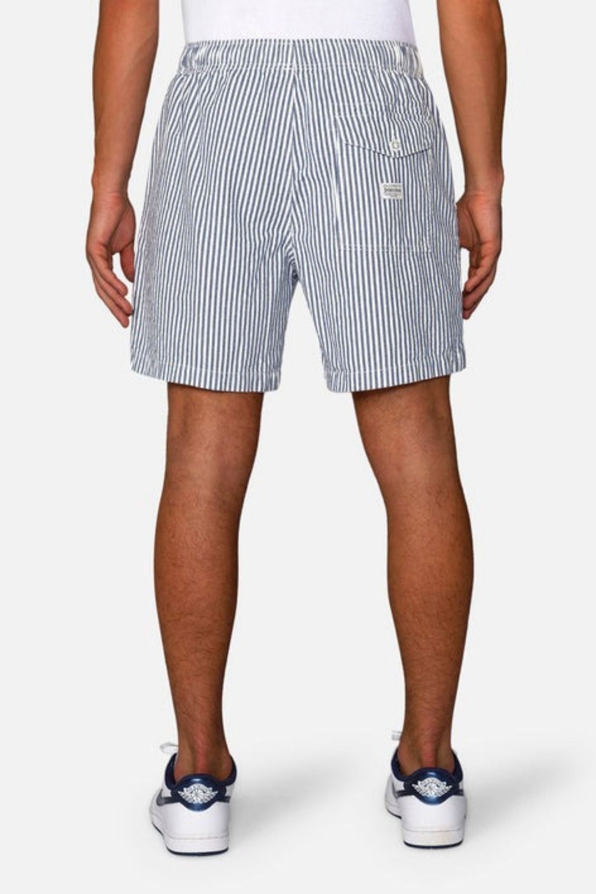 Rear view of a person wearing blue and white Industrie The New Southwest Short, featuring an elasticated waistband, paired with white socks and sneakers with blue accents, standing against a plain background.