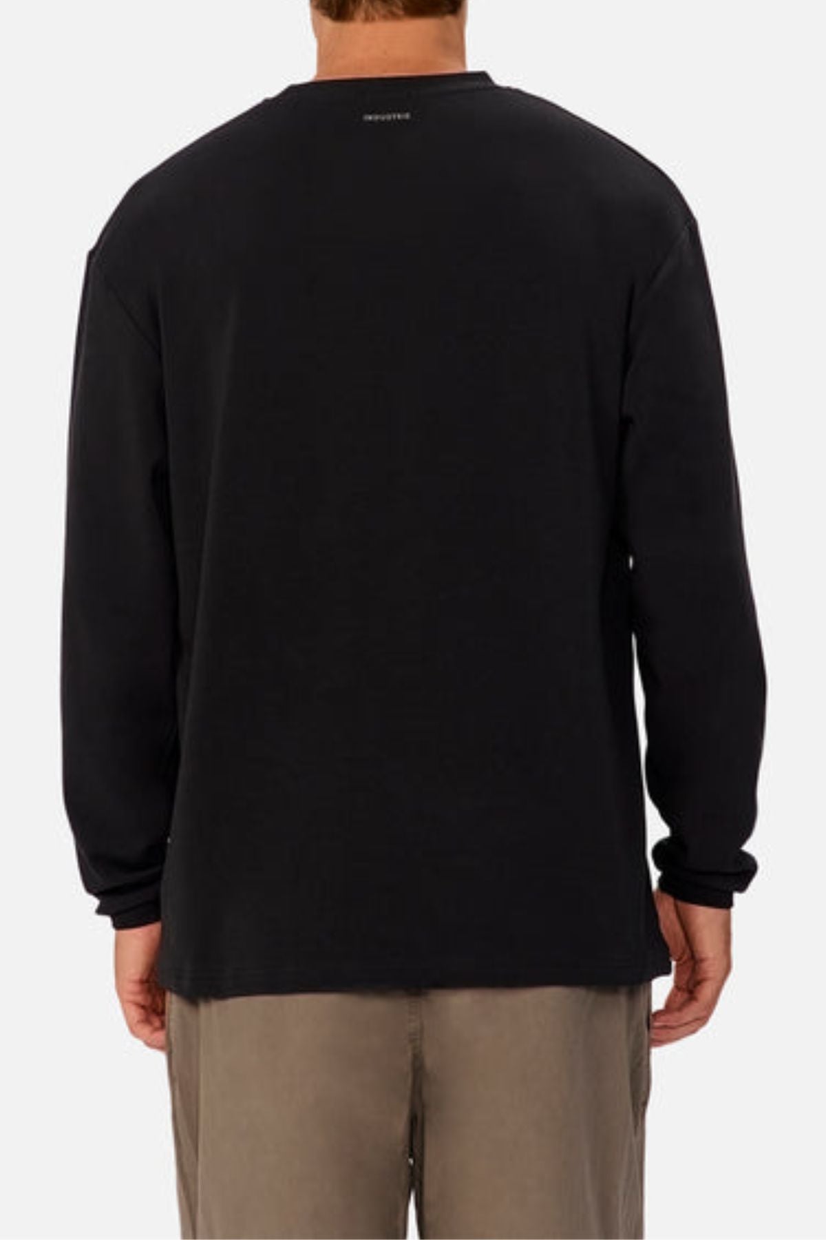 A person is shown from the back wearing an oversized black Industrie The Newport Long Sleeve Tee with a heavyweight finish, featuring small white text near the neck on the upper back, paired with light brown pants against a plain white background.