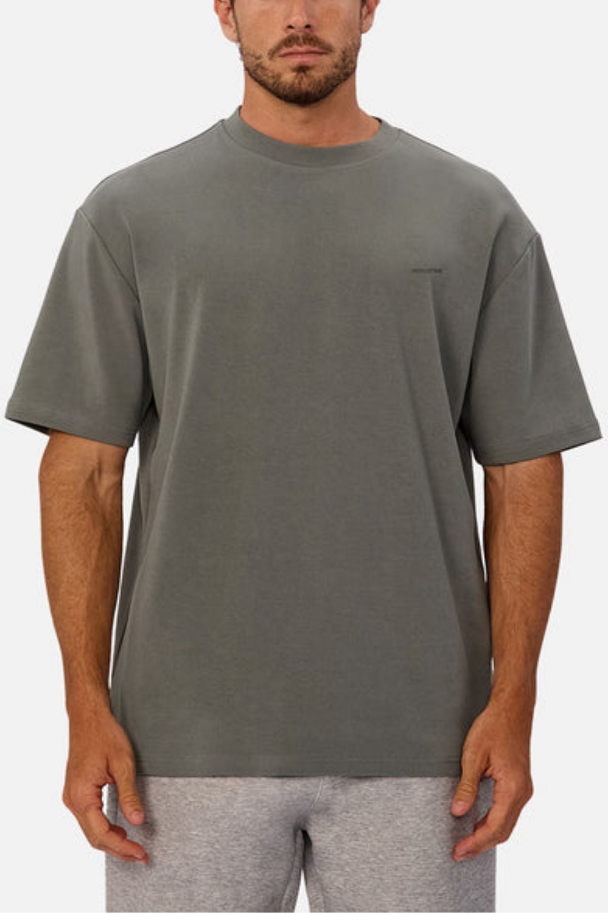 A man wears the Industrie The Newport Tee, showcasing an oversized fit and heavyweight fabric. He stands facing forward in plain gray and light gray shorts against a white background with his arms relaxed at his sides.