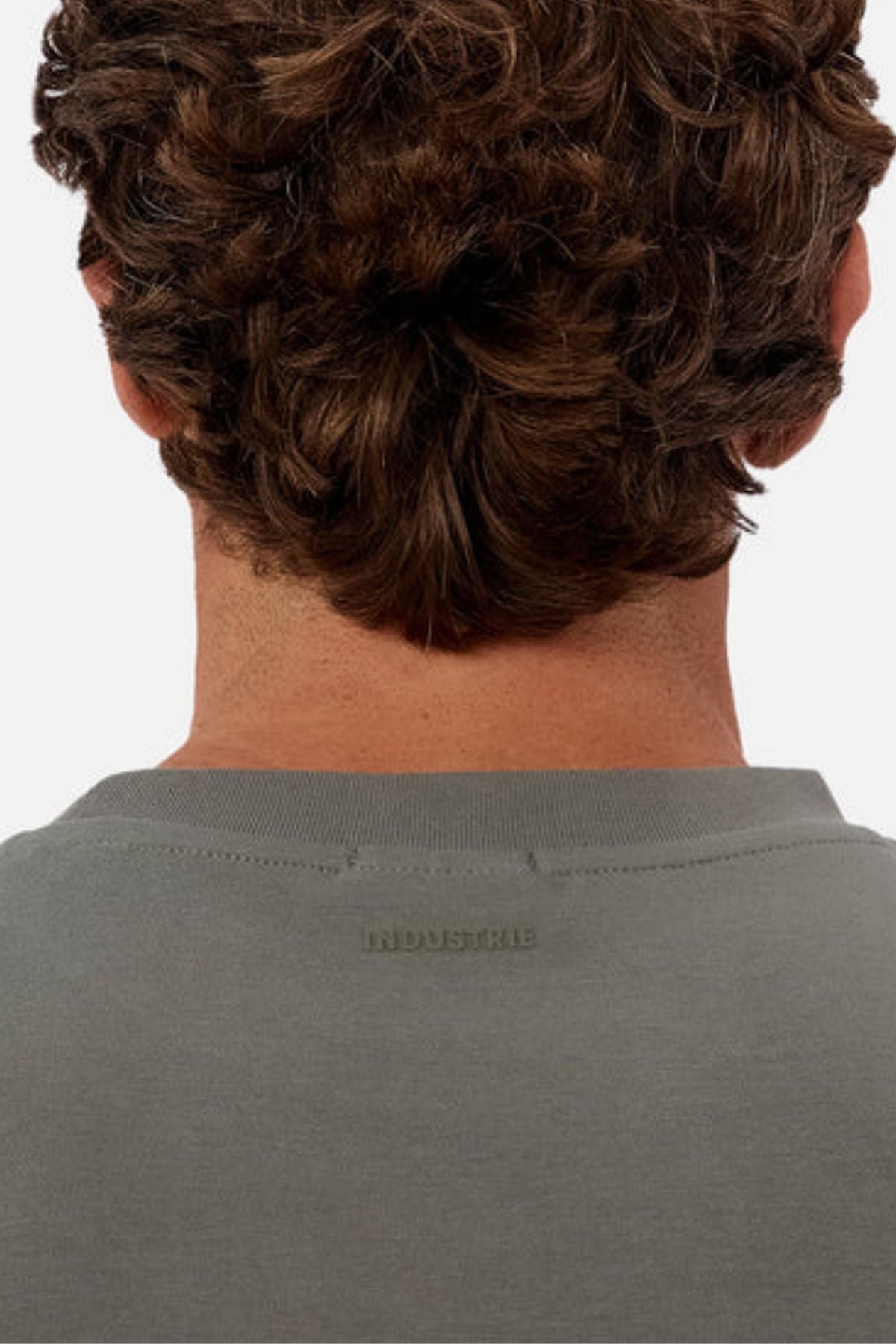 The back view of a person with short, curly brown hair wearing the Industrie The Newport Tee in grey. The image highlights the upper back and neck, showcasing its heavyweight fabric and subtle embossed text.