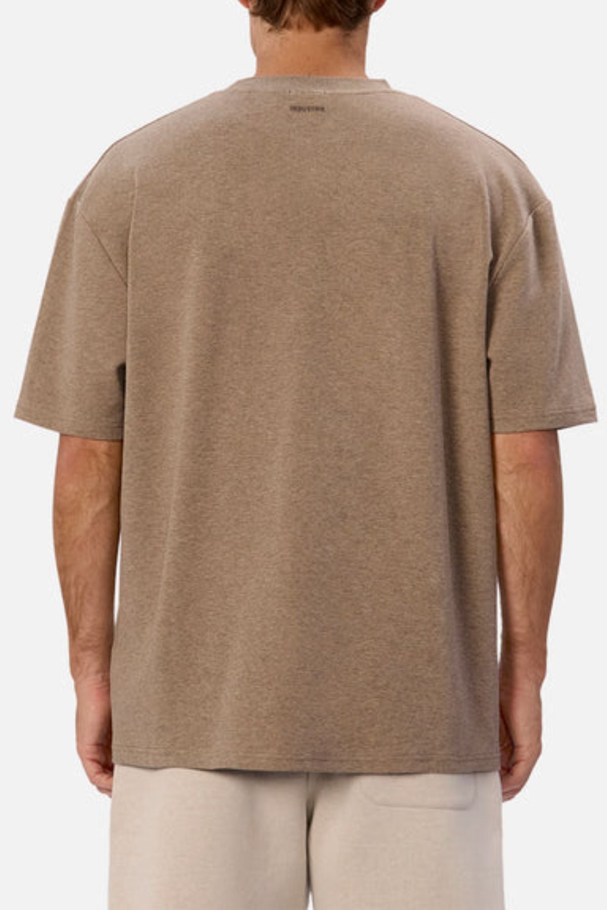 A person wearing Industrie's The Newport Tee in brown paired with light-colored shorts is turned away from the camera. The oversized fit of this 100% cotton tee enhances a relaxed vibe against the simplistic white backdrop.