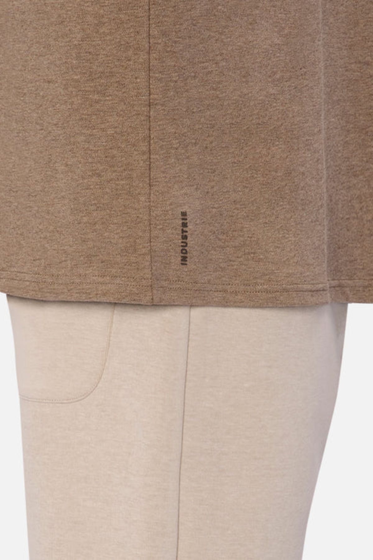 A close-up of someone wearing Industrie The Newport Tee with an oversized fit, in a brown shade featuring a small black logo near the hem, paired with light beige pants. The texture of the 100% cotton clothing is soft and casual.