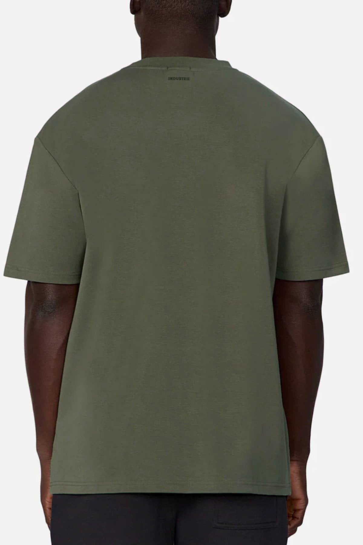 A person is shown from behind wearing an oversized Industrie The Newport Tee in olive green, made of 100% cotton, against a plain light background. The shirt features a simple design with no visible graphics or logos.