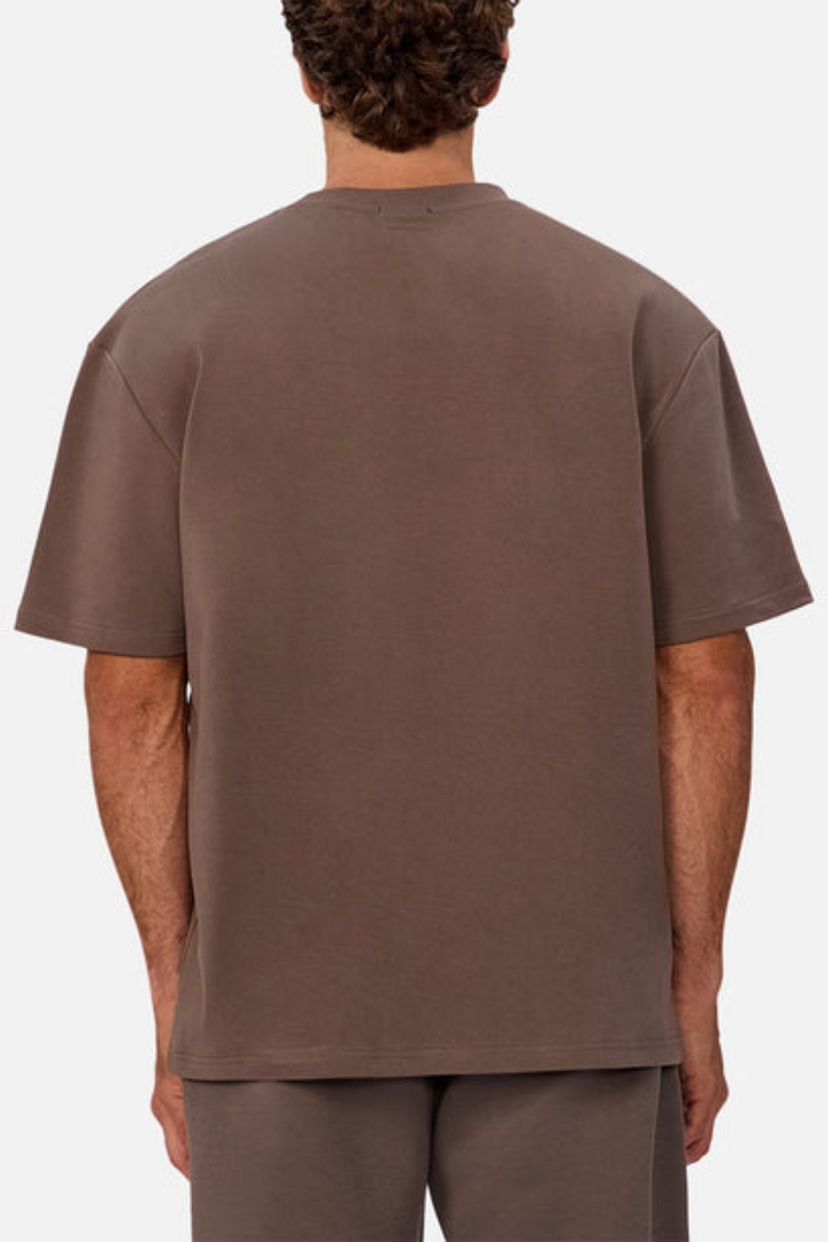 A person with short curly hair is shown from behind, wearing an oversized Industrie The Newport Tee and matching brown shorts against a plain, light background.