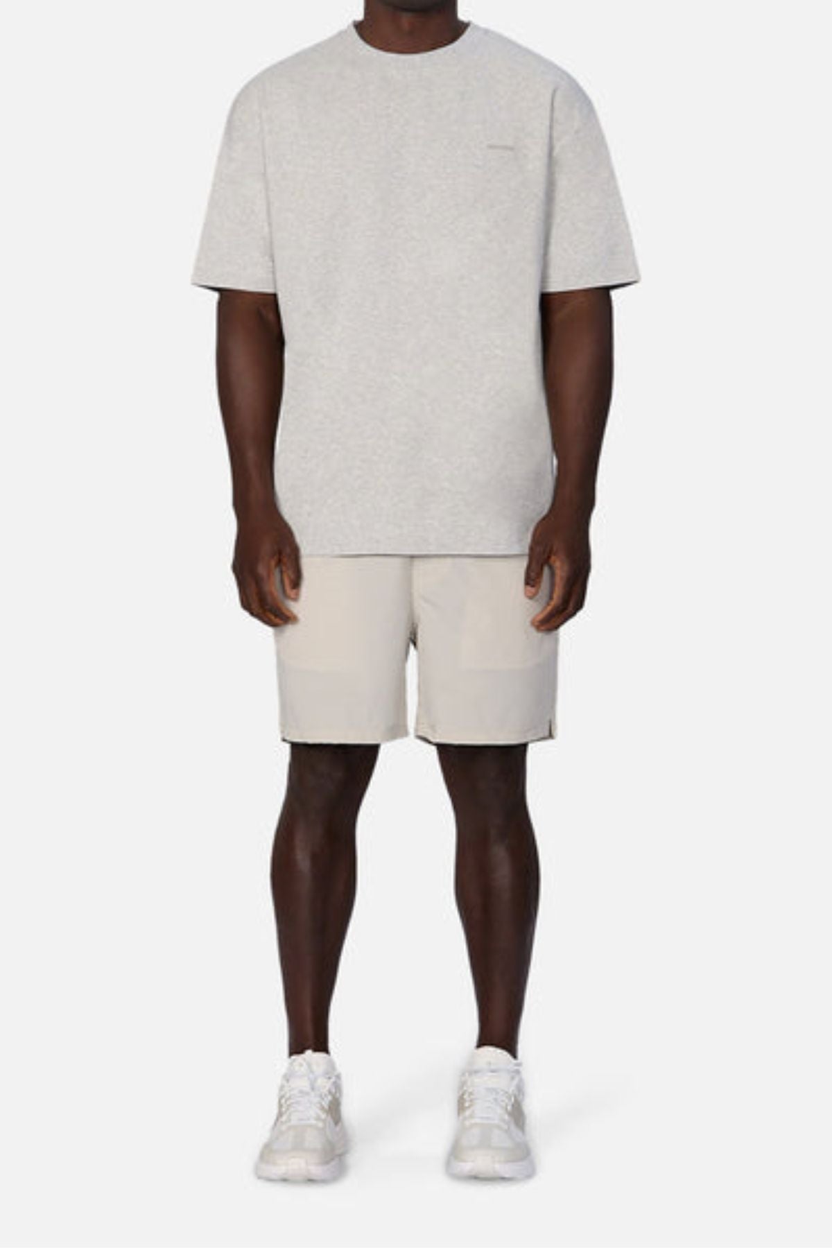 A person dressed in Industrie The Newport Tee, an oversized fit light gray T-shirt, paired with beige shorts and white sneakers stands against a plain white background. This 100% cotton outfit looks casual and comfortable.