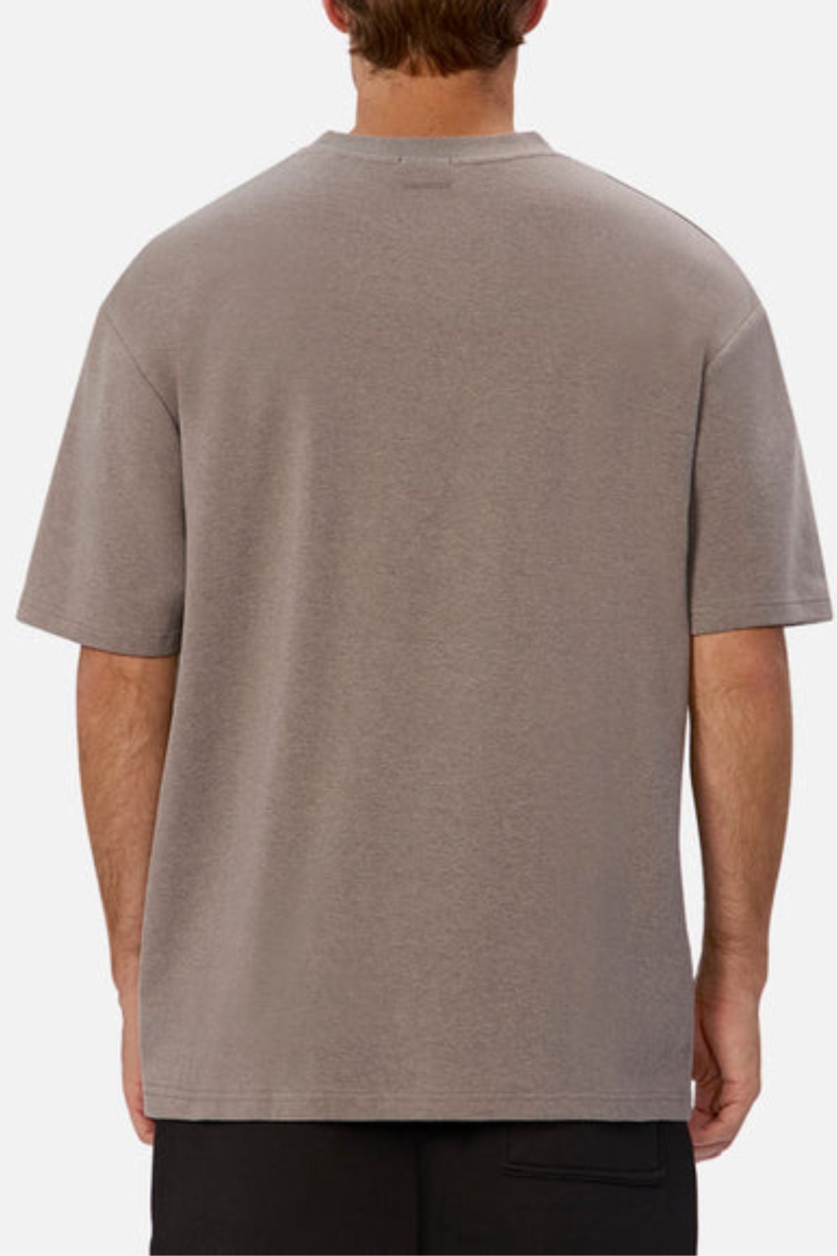 A person wearing an oversized fit gray T-shirt, similar to the Industrie The Newport Tee, stands with their back to the camera. The background is plain and minimalistic.