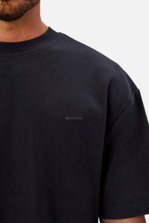 A man wears the Industrie The Newport Tee, made from heavyweight fabric with an oversized fit. "INDUSTRIE" is subtly printed on the chest, and only the lower half of his face and upper torso are visible.