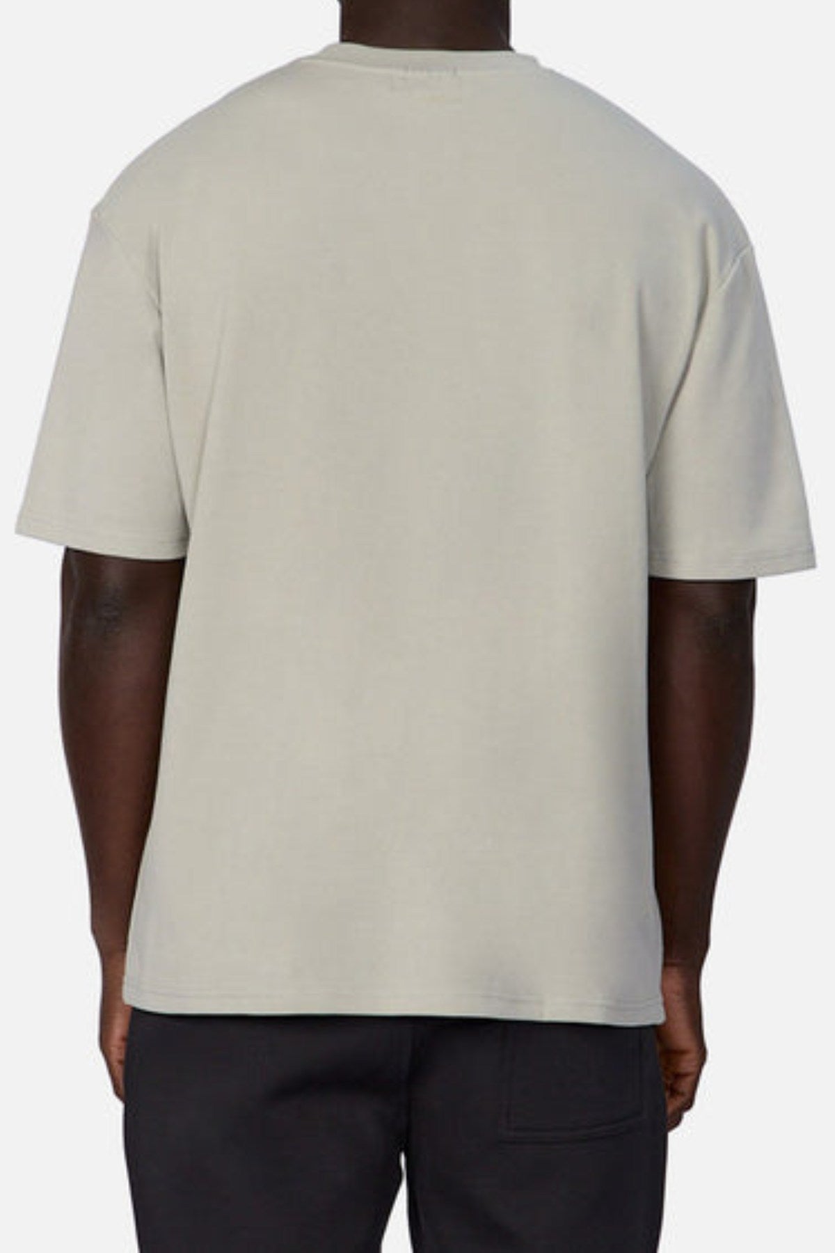 A person stands with their back to the camera, wearing Industrie's The Newport Tee in light gray and dark pants against a gray backdrop. The oversized tee is made from heavyweight fabric, showcasing the stylish back view of this casual outfit.