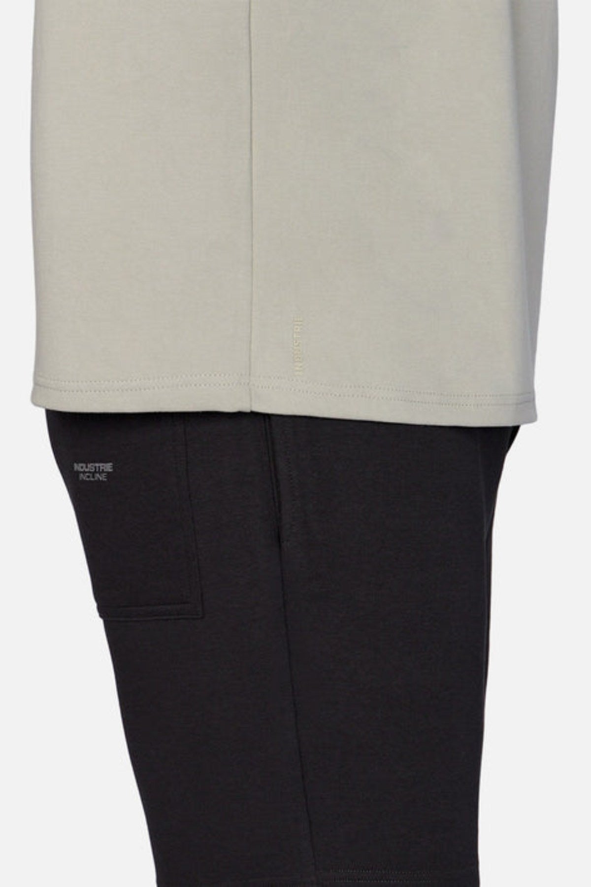 A close-up side view shows someone in an oversized fit light gray shirt with black pants, displaying "INDUSTRIE RECINE" above a small pocket. The focus is on heavyweight fabric and overlapping layers, echoing the style of Industrie's The Newport Tee.