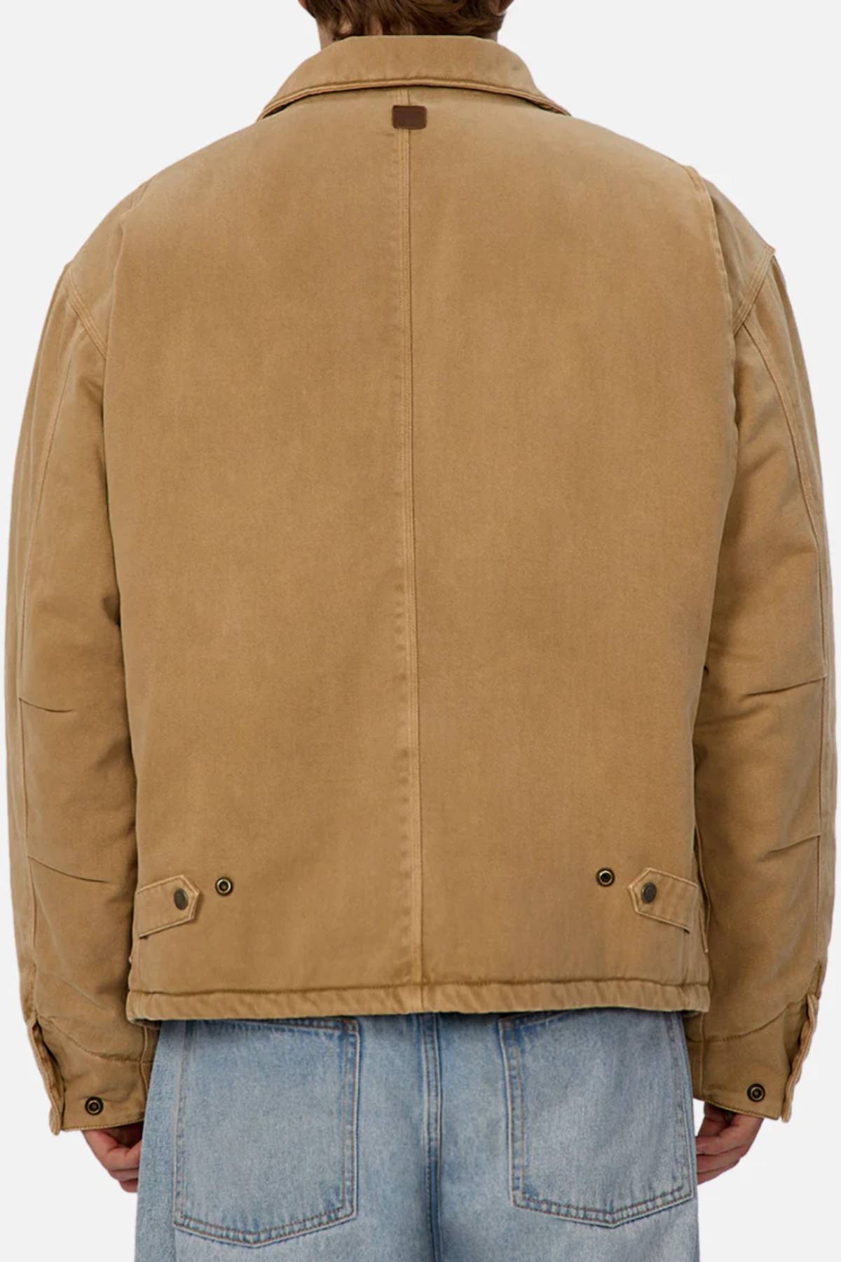 A person is seen from the back wearing the Industrie The Oklahoma Jacket in light brown with blue jeans. The jacket has a collar, adjustable buttoned flaps at the waist, and their hair is visible above the collar.