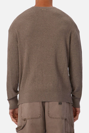 Someone is shown from the back wearing the Industrie The Philly Waffle Knit sweater in taupe with long sleeves, a crew neck, and loose-fitting taupe pants against a plain background.