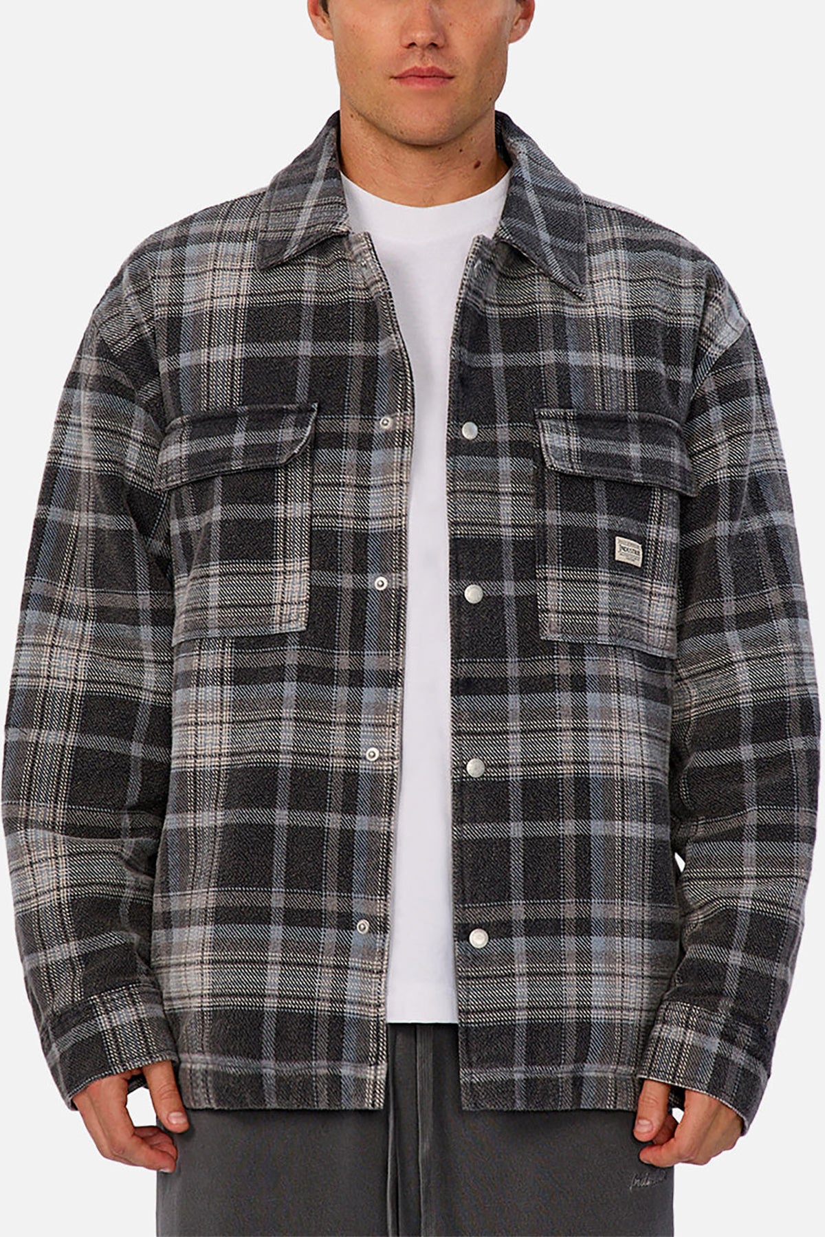Someone wears the Industrie The Phoenix Jacket—a plaid shirt jacket in gray, black, and white with a heavyweight feel—over a white T-shirt and dark pants, standing against a plain background.