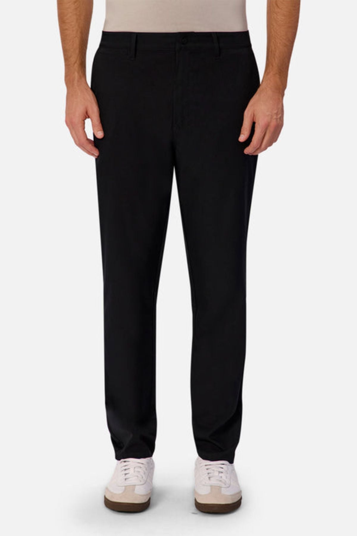 A person wearing the Industrie The Tech Pinehurst Chino Pant in black recycled polyester and white sneakers stands against a neutral background. The straight-cut trousers offer flexibility, complemented by a light-colored shirt tucked neatly into the waistband.