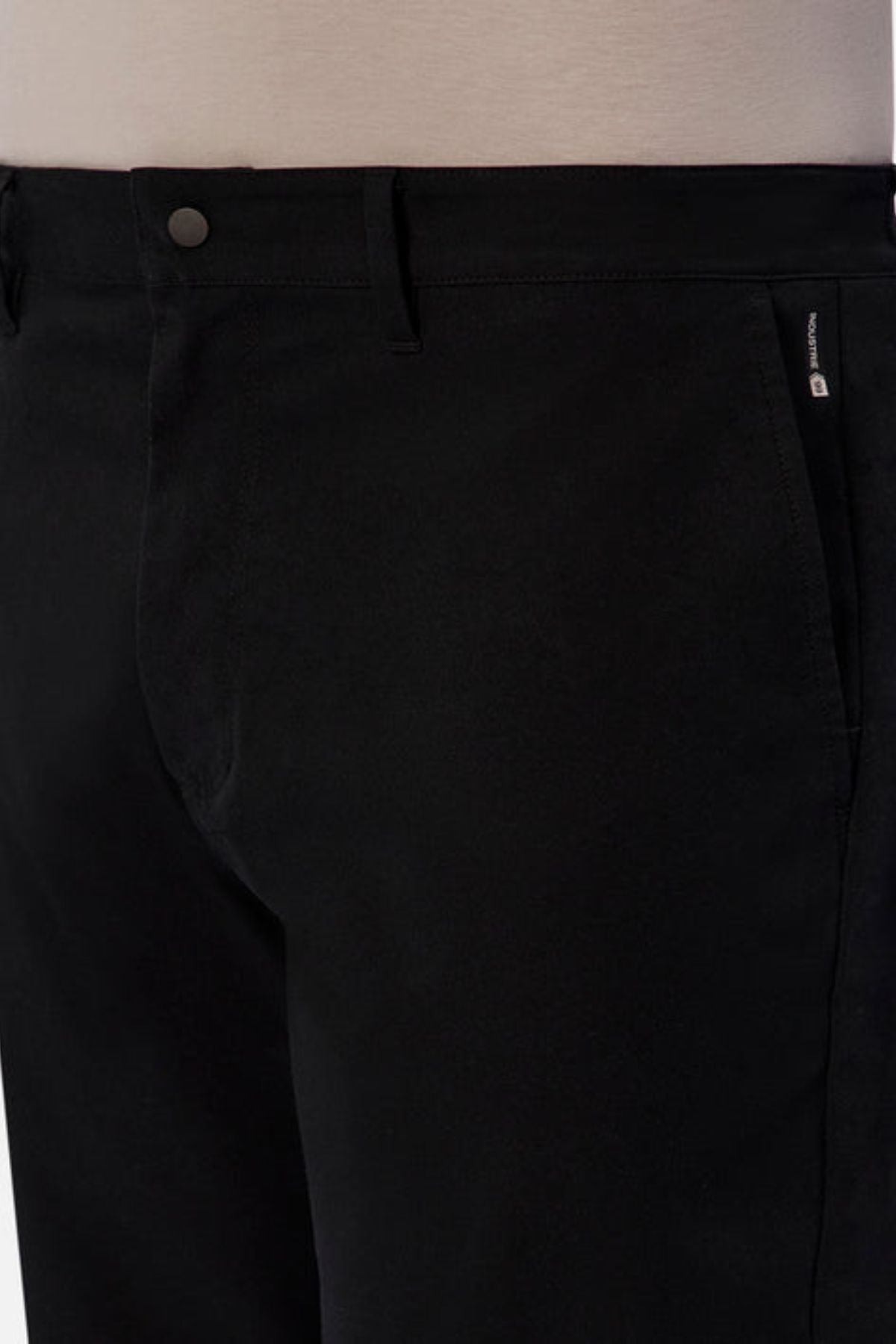 Close-up of a person wearing Industrie The Tech Pinehurst Chino Pant in black. The smooth fabric, crafted from recycled polyester for extra flexibility, features a small visible zipper on the side. Belt loops and a single button closure accentuate the garment's design against a neutral background.