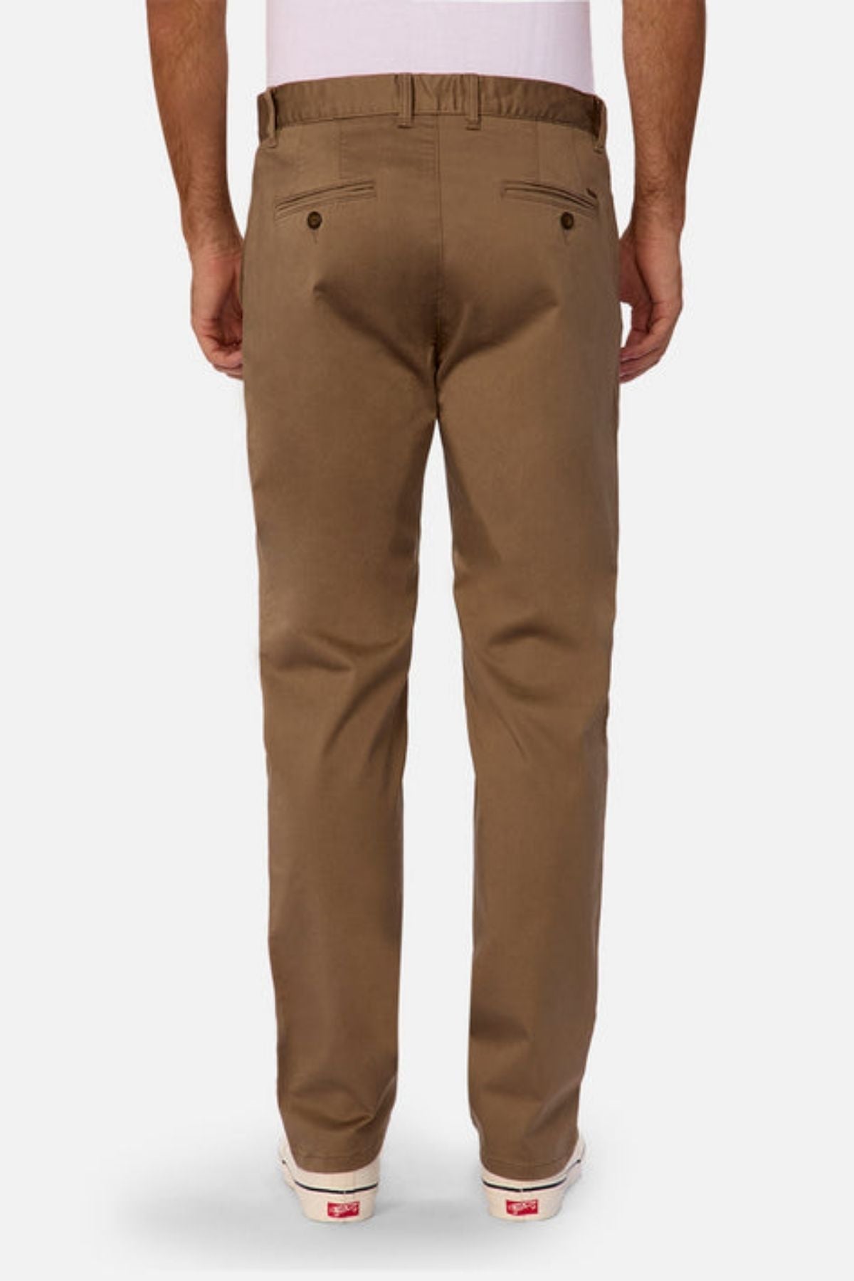 A man is seen from behind wearing Industrie The Regular Cuba Chino Pant in brown with a wider leg fit, belt loops, and two back pockets with button closures, paired with a white shirt and white sneakers.