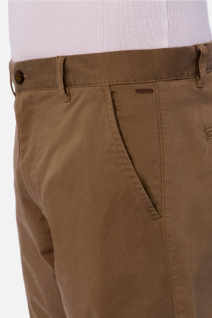 A close-up of a person wearing Industrie The Regular Cuba Chino Pant in light brown with a white shirt tucked in, focusing on the front pocket and waistband to showcase its comfortable stretch cotton blend fabric.