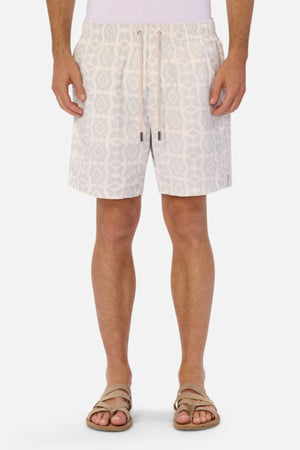 A person wearing the Industrie The Saratoga Swim Short, known for its unique print, stands against a plain white background. They complement the vibrant design with beige sandals, while the quick-drying fabric guarantees both comfort and style. Their torso is not visible.