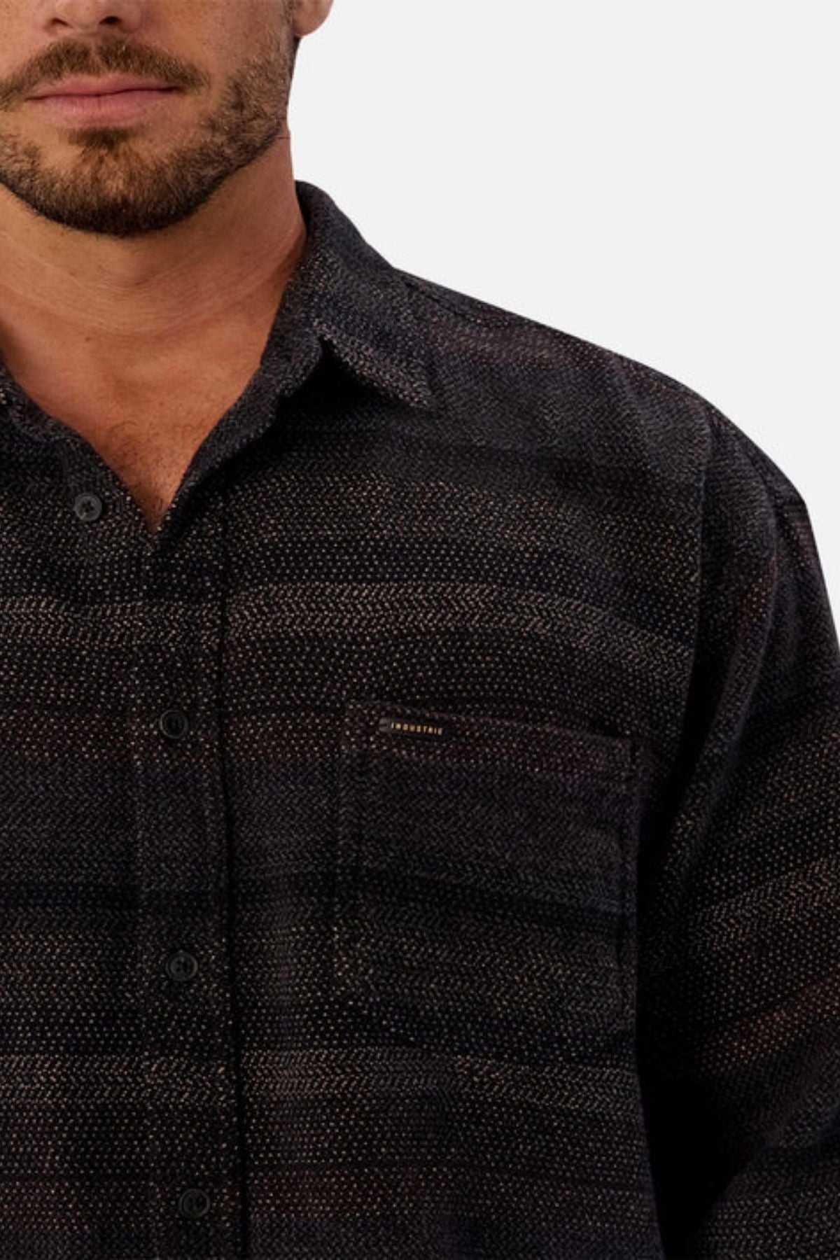 A man with a short beard models the Industrie The Sonoran Long Sleeve Shirt—a regular fit, dark button-up with a shadow pattern and chest pocket—shown from shoulders up against a plain white background.