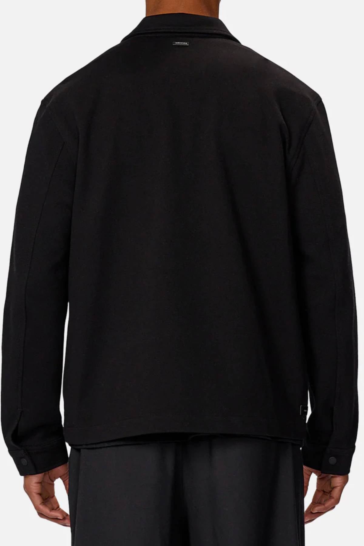 A person is shown from the back against a plain light background wearing black pants and the Industrie The Southport Jacket, a long-sleeved black jacket with a front zip closure and an Industrie logo tag at the upper center near the collar.