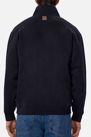 A person is shown from the back against a plain light background, wearing blue jeans and Industrie The Staunton Track Top, which features a small brown patch near the collar.
