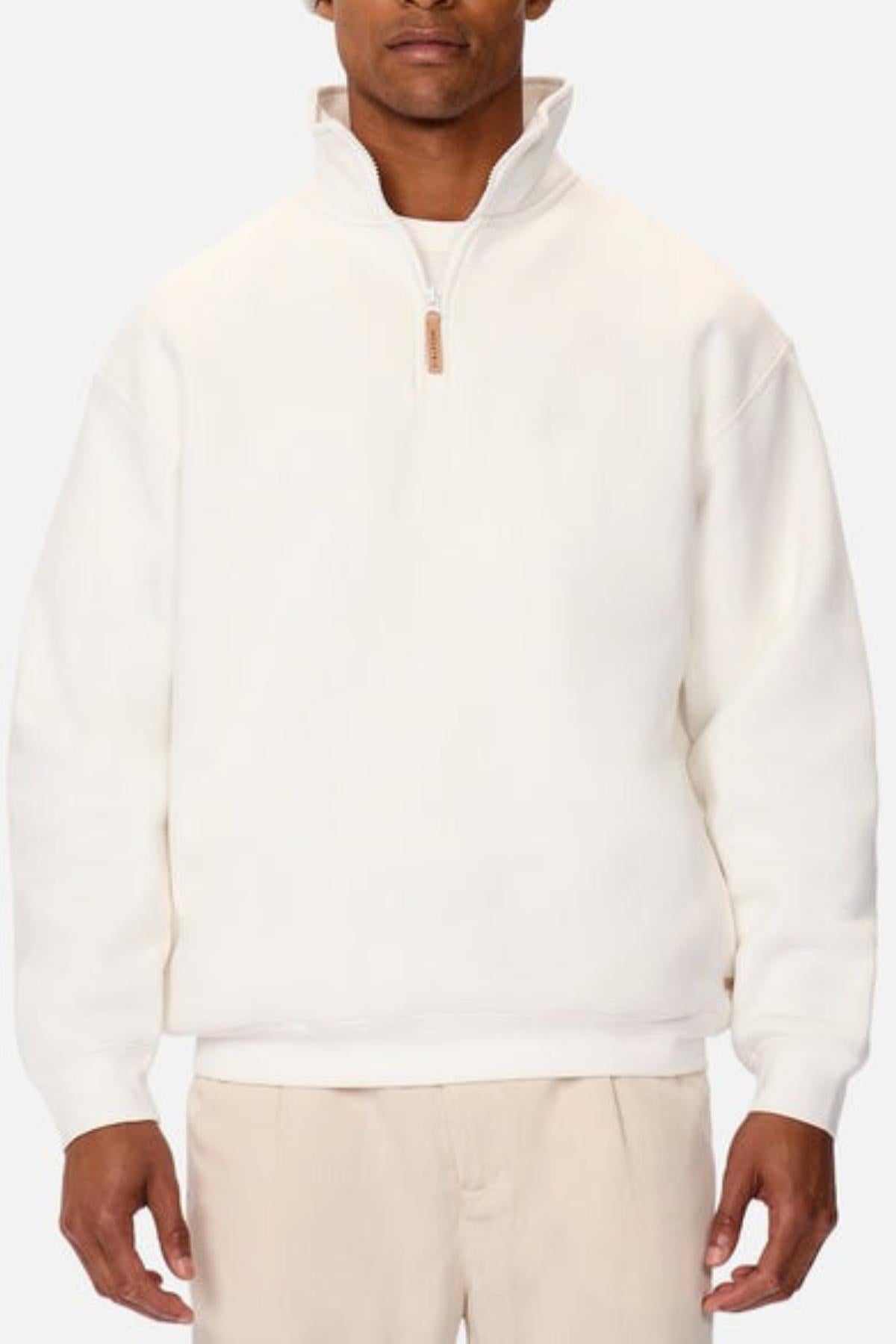 A man wears the Industrie The Staunton Tracktop, a white quarter-zip sweatshirt with branded trims and a high collar. Its relaxed fit and soft fleece lining provide comfort and style as he faces forward against a plain background.