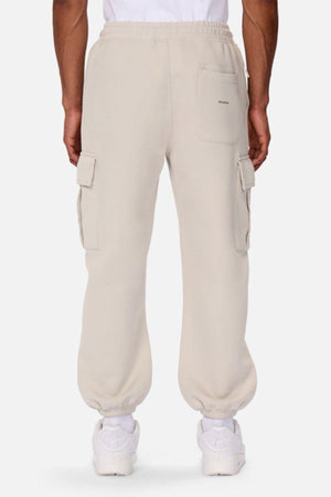 A person is seen from behind wearing Industrie The Tech Combat Trackpant in light beige with elastic cuffs, rear and side flap pockets, styled with white sneakers and a white T-shirt for a modern athletic look.