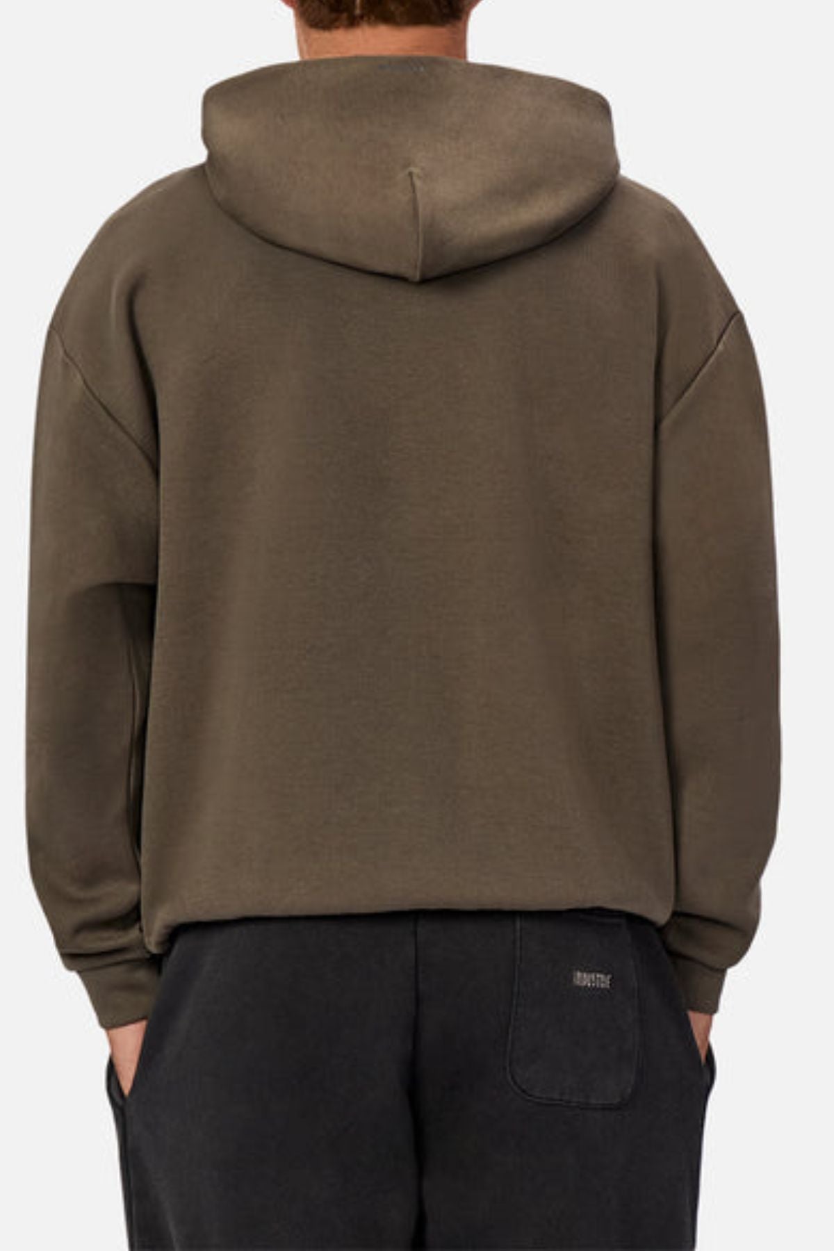 A person stands with their back to the camera, wearing the Industrie The Tech Del Sur Hood and dark pants. Their hands are in their pockets, set against a plain white background.