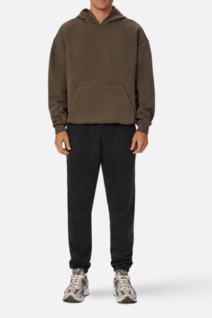 A person stands facing forward in the Industrie The Tech Del Sur Hood, featuring high density print and advanced athletic fabric, paired with black sweatpants and gray sneakers. The plain white background highlights the modern look; their head is partially out of frame.