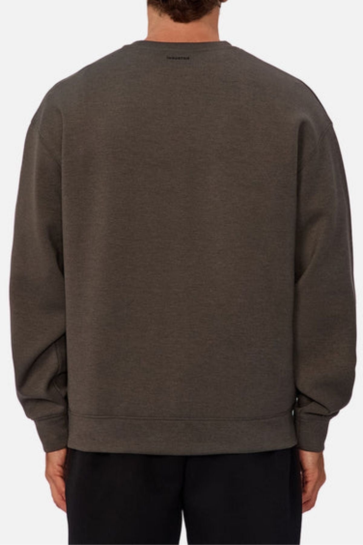 A person is seen from behind in a loose-fitting, dark gray Industrie The Tech Del Sur Sweat with long sleeves, breathable fabric, and a subtle back neck logo, paired with black pants against a plain light-colored background.