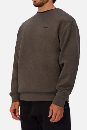 A man is wearing the Industrie The Tech Del Sur Sweat, a loose-fitting, dark gray athleisure sweatshirt with long sleeves, paired with black pants. He stands against a white background with only his upper body and part of his face visible.