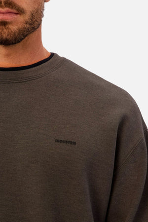 A close-up of a man wearing the Industrie The Tech Del Sur Sweat in dark grey, featuring "INDUSTRIE" embroidered in small black letters on the left chest. Only the lower half of his face and upper torso are visible.