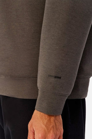 Someone is shown from the shoulders down wearing the Industrie The Tech Del Sur Sweat, a grey athleisure sweatshirt with "INDUSTRIE" printed near the wrist, paired with black pants and their left arm relaxed at their side.