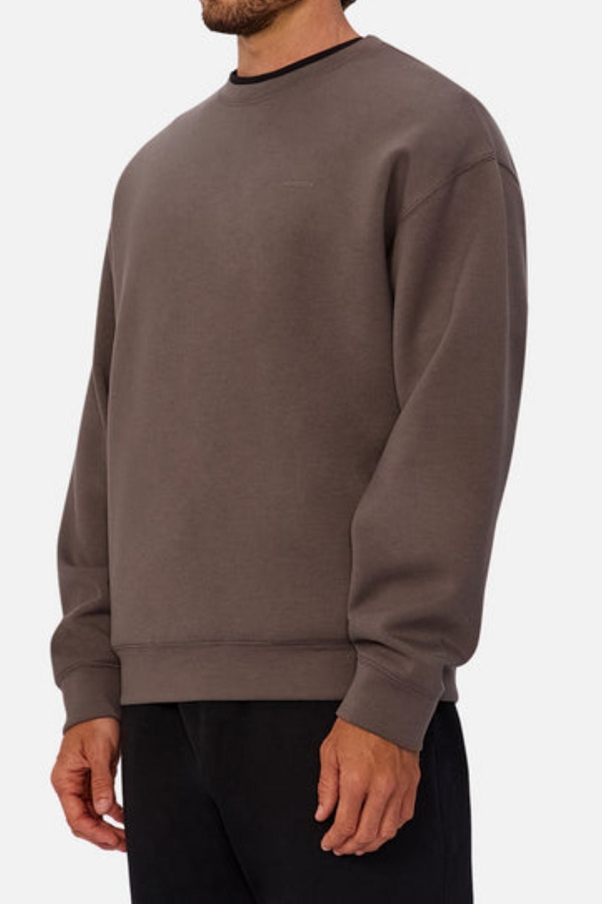 A man, shown from the shoulders down against a plain light background, wears the Industrie The Tech Del Sur Sweat—a loose-fitting, long-sleeve sweatshirt in dark gray with modern athleisure style—paired with black pants.