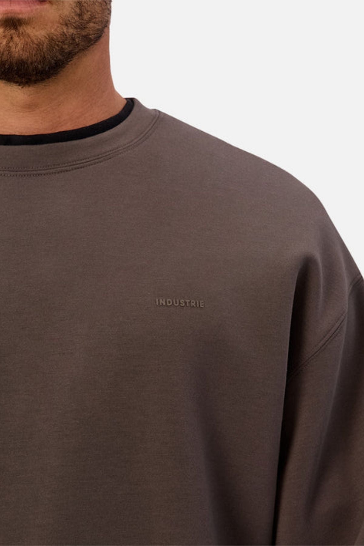 A close-up of someone wearing the Industrie The Tech Del Sur Sweat, showcasing its modern athleisure style and subtle "INDUSTRIE" chest embroidery, with only a partial view of the wearer’s face.