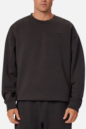 Wearing the Industrie The Tech Del Sur Sweat in plain black with matching stretch pants, a person stands against a light background. Their face is partially hidden, showcasing modern athleisure style and 4-way stretch comfort.