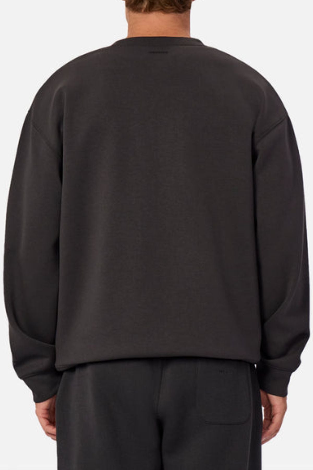 A person stands with their back to the camera in the Industrie The Tech Del Sur Sweat and matching pants. This modern athleisure set offers 4-way stretch comfort, shown against a plain, light-toned background.