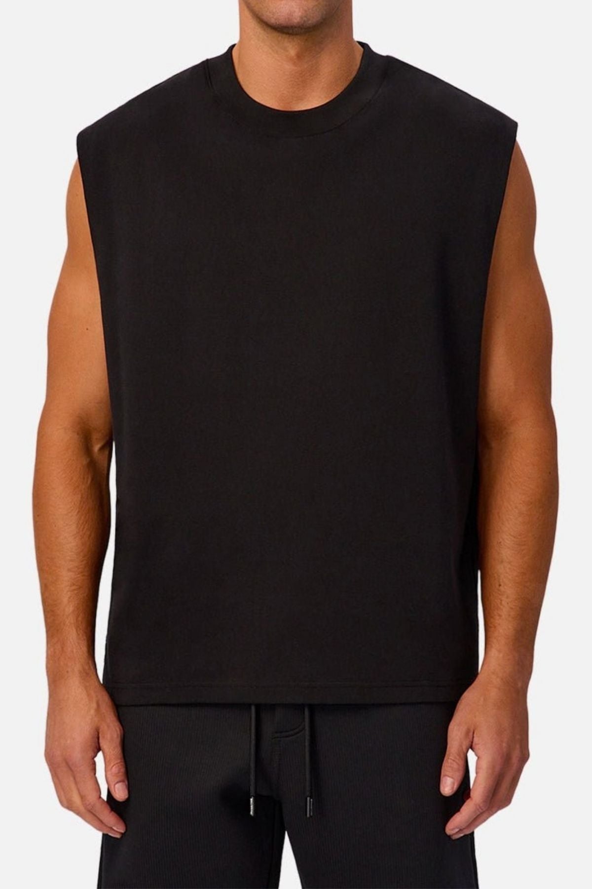 A man wearing the Industrie The Tech Port Sleeveless Tee and black pants stands against a plain light background. His arms are relaxed at his sides, and his face is not visible.