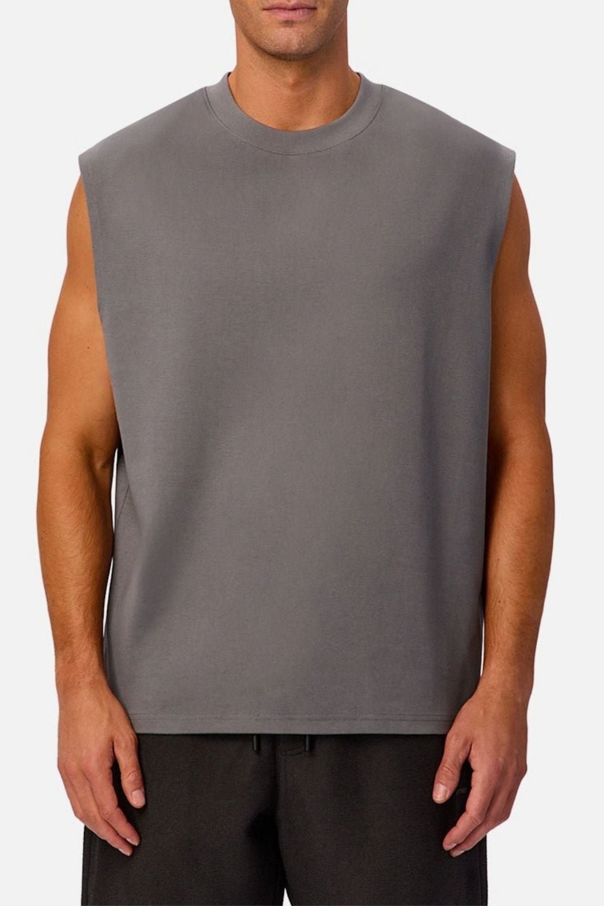 A man stands against a plain white background wearing the Industrie The Tech Port Sleeveless Tee in gray, its relaxed fit and tech material complementing his casual stance as he pairs it with black shorts, arms resting comfortably at his sides.