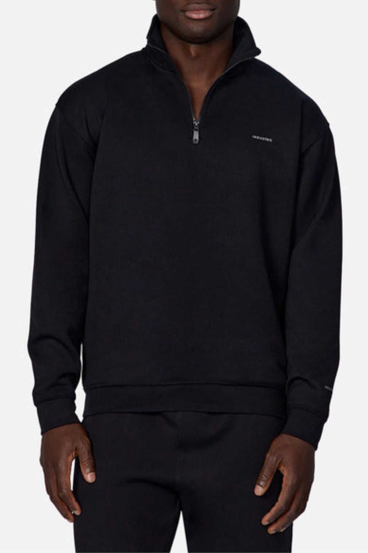 A man in the Industrie The Tech Staunton Track Top and matching black pants, both with a small left chest logo, stands against a plain light background.