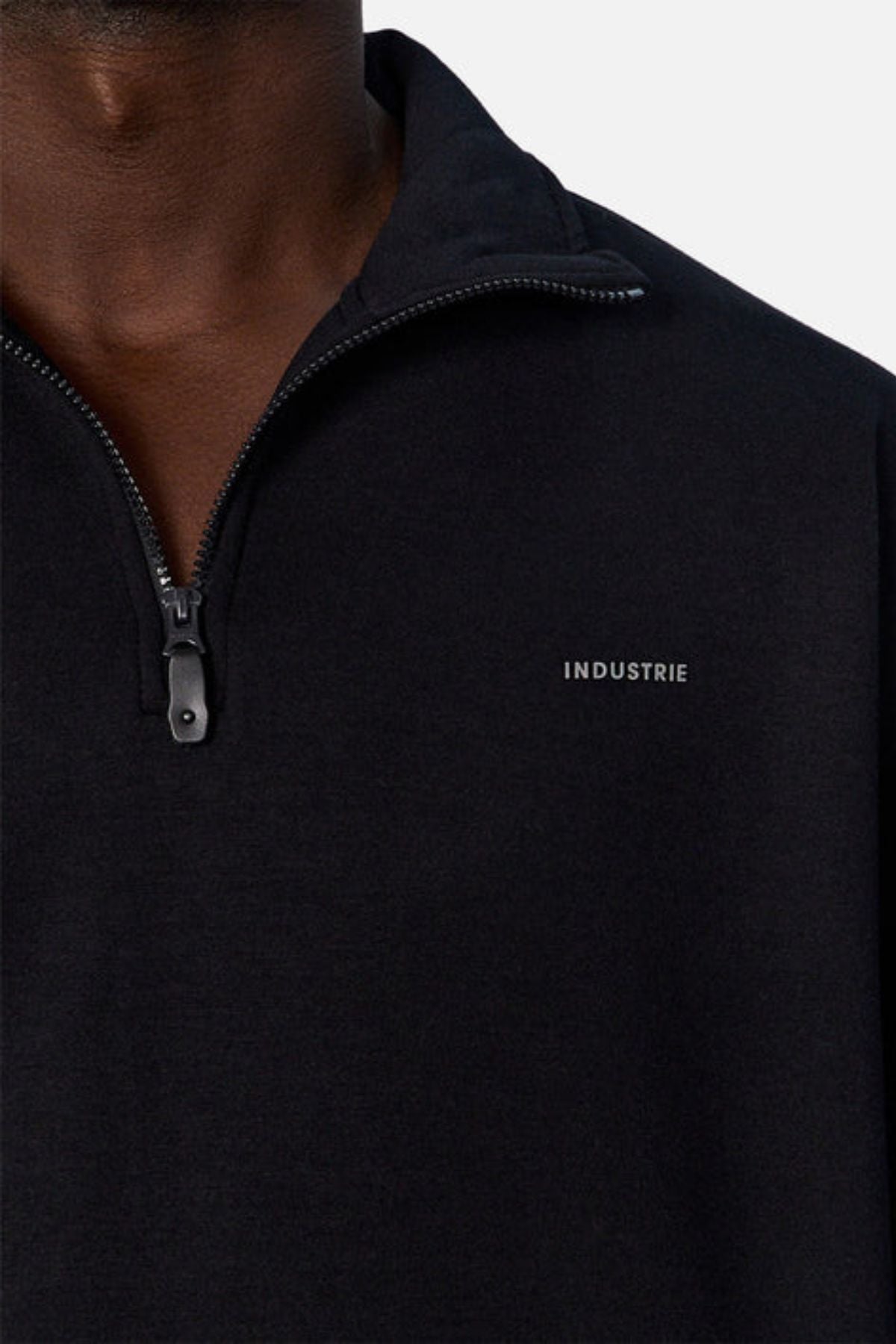 A close-up of a person wearing the Industrie The Tech Staunton Track Top in black, featuring "INDUSTRIE" in small white letters on the left chest and a partially open zipper, highlighting its premium athletic fabric against a plain white background.