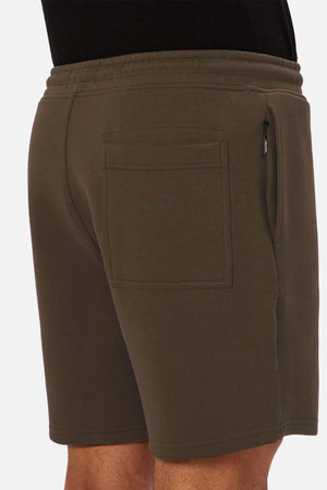 A person is wearing the Industrie The Tech Track Short in olive green, featuring an elastic waistband, side zip pocket, and a back pocket with a subtle “INDUSTRIE” logo. Only the lower torso and thighs are visible.