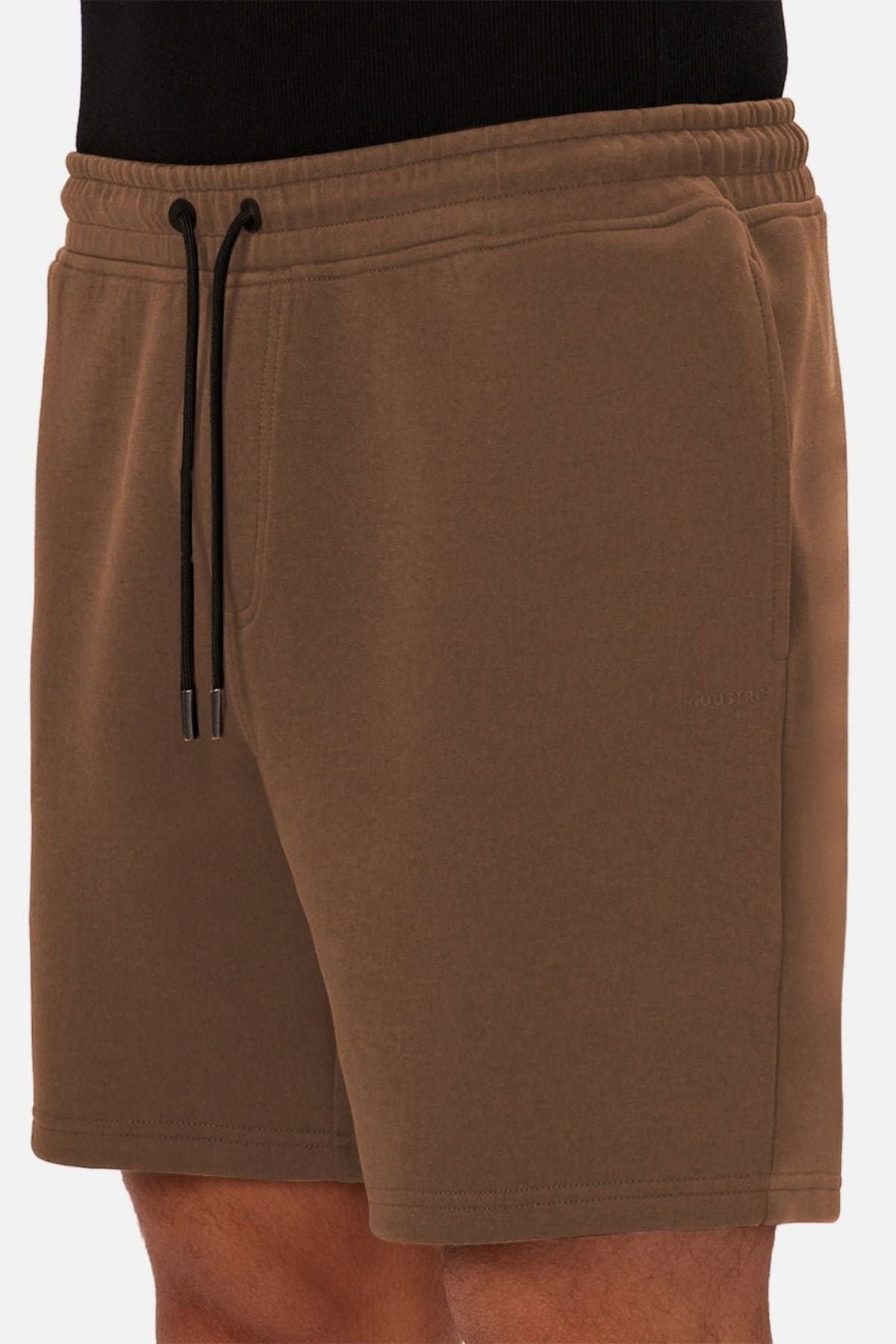 A person wearing the Industrie The Tech Track Short in brown, featuring a drawstring waist, side pockets, and a black waistband, shown from the waist to mid-thigh against a plain background.