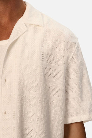 Close-up of a person wearing the Industrie The Venty Short Sleeve Shirt, a lightweight cotton shirt with a checkered texture, soft collar, and visible buttons over a white ribbed undershirt. Only the upper body is visible.