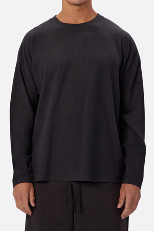 Wearing the Industrie The Waffle Long Sleeve Tee in black with matching black pants, a person stands against a plain light background. Their face is not shown in the image.