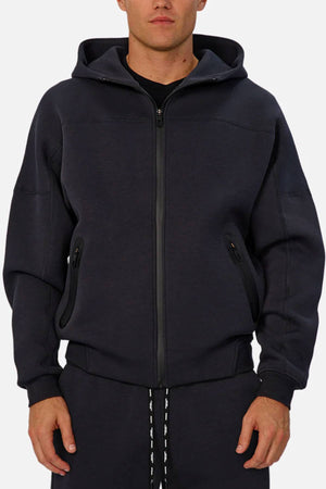 A man in the Industrie The Washington Zip Thru jacket with a hood and matching joggers stands facing forward, hands relaxed at his sides—making this look ideal for everyday style.